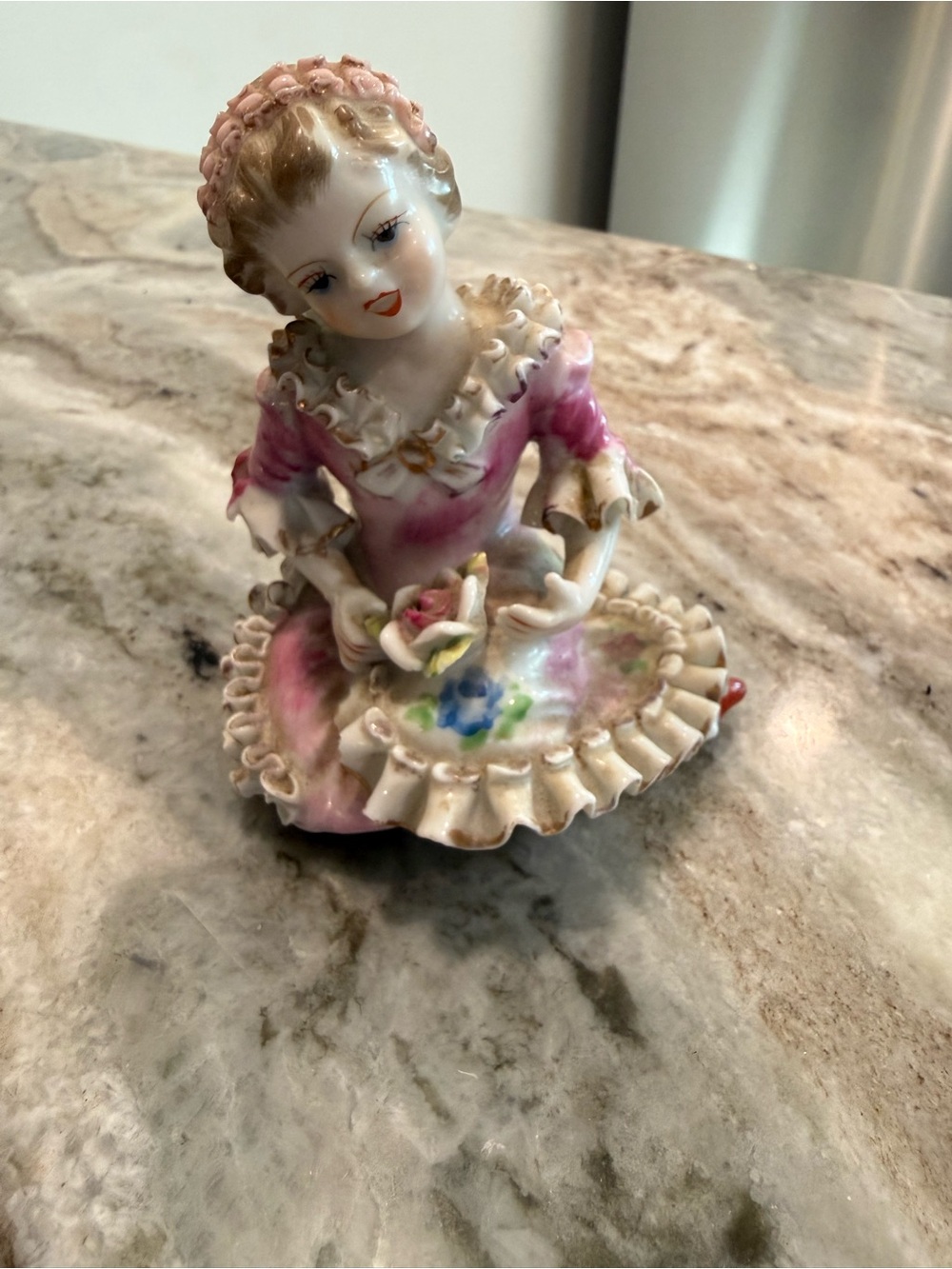 A delicate porcelain figurine depicting a woman in a pink dress with intricate